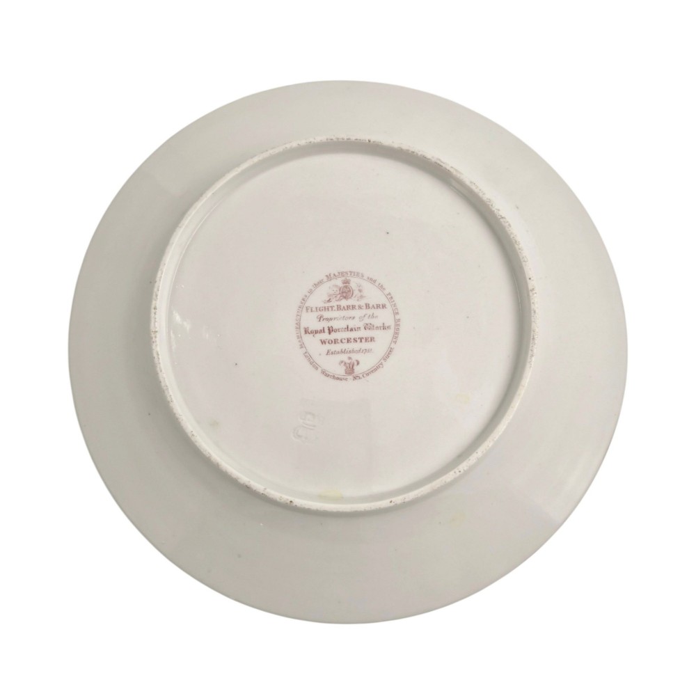 A circular white porcelain plate featuring a gilded rim, a red and pink floral border, and a central armorial crest of a bird beneath a coronet with a banner reading STRIKE. View IV