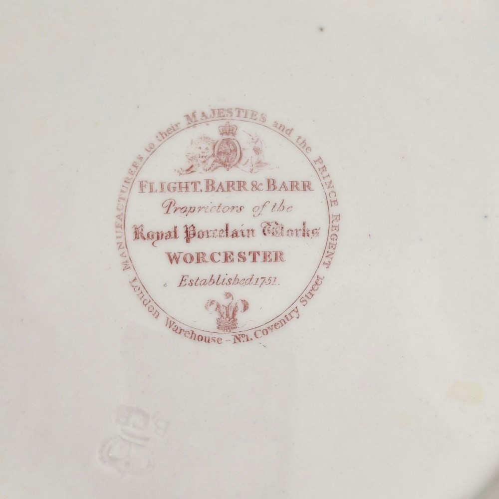 A circular white porcelain plate featuring a gilded rim, a red and pink floral border, and a central armorial crest of a bird beneath a coronet with a banner reading STRIKE. View V