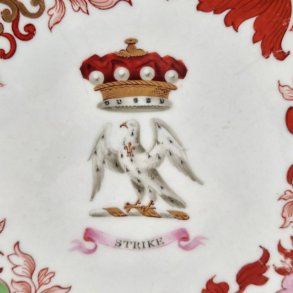 A circular white porcelain plate featuring a gilded rim, a red and pink floral border, and a central armorial crest of a bird beneath a coronet with a banner reading STRIKE. View VII