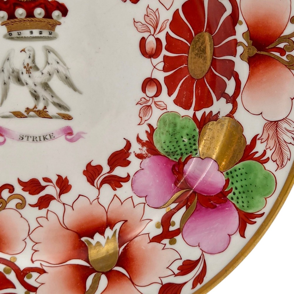 A circular white porcelain plate featuring a gilded rim, a red and pink floral border, and a central armorial crest of a bird beneath a coronet with a banner reading STRIKE. View VIII
