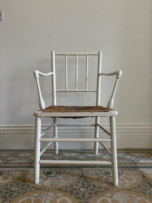 fig 3. A white painted 19th-century turned wood armchair with a spindle back, curved armrests, and a natural woven rush seat.