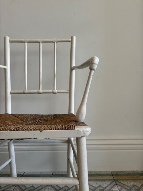 fig 4. A white painted 19th-century turned wood armchair with a spindle back, curved armrests, and a natural woven rush seat.