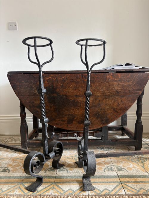 fig 1. A pair of tall 19th-century black wrought iron fire dogs featuring hand-twisted shafts, scrollwork feet, and circular top ring terminals.