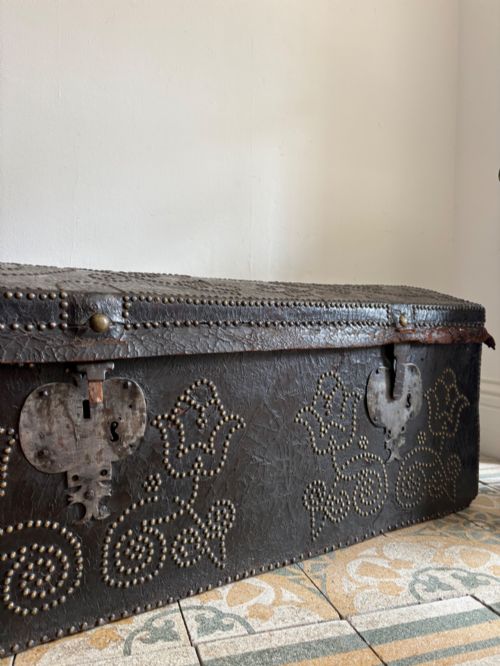 fig 1. An 18th-century Dutch dark brown leather trunk featuring a domed lid, intricate brass studding in scrolling floral patterns, and iron lock hardware.
