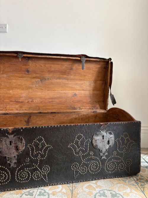 fig 2. An 18th-century Dutch dark brown leather trunk featuring a domed lid, intricate brass studding in scrolling floral patterns, and iron lock hardware.
