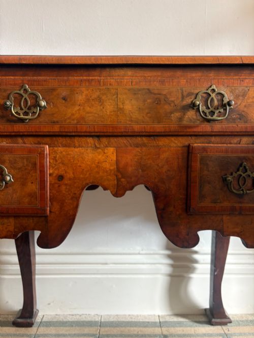 fig 2. An early 18th-century figured walnut lowboy side table featuring three drawers, a shaped apron, brass handles, and cabriole legs.