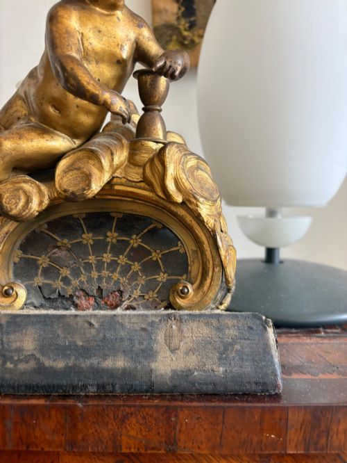 fig 1. A late eighteenth or nineteenth-century French gilt bronze ormolu sculpture featuring a reclining putto holding a small vessel above a scrolled arch base.
