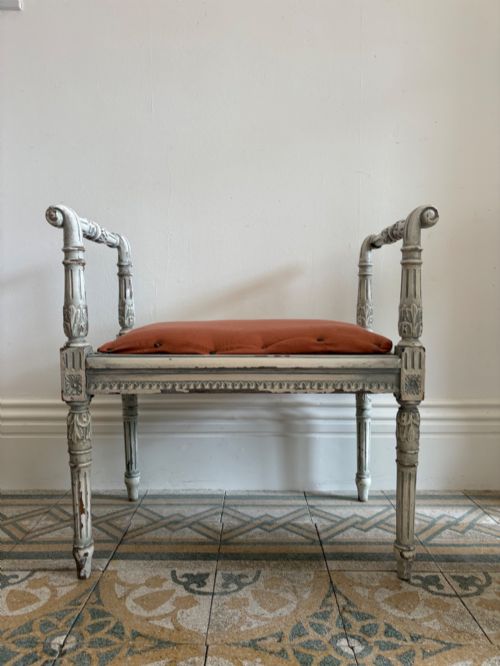 fig 1. A white painted Gustavian style stool featuring raised side handles, fluted legs, and a terracotta silk upholstered seat.