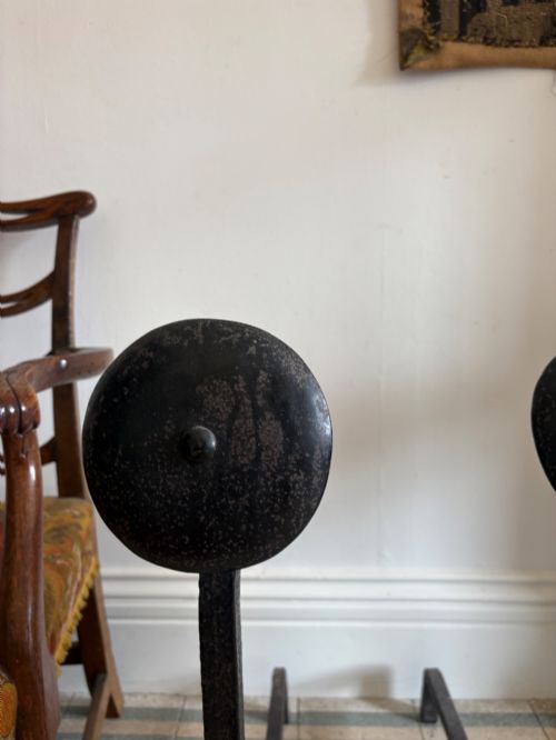 fig 2. A pair of hand-forged black wrought iron fire dogs featuring circular disc tops, tool hooks, and scrolled arched feet.