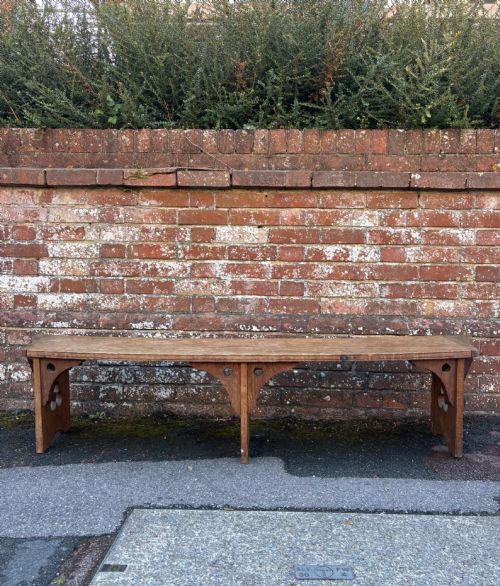 fig 1. A long curved oak bench featuring trefoil carved cut-outs on the end supports.