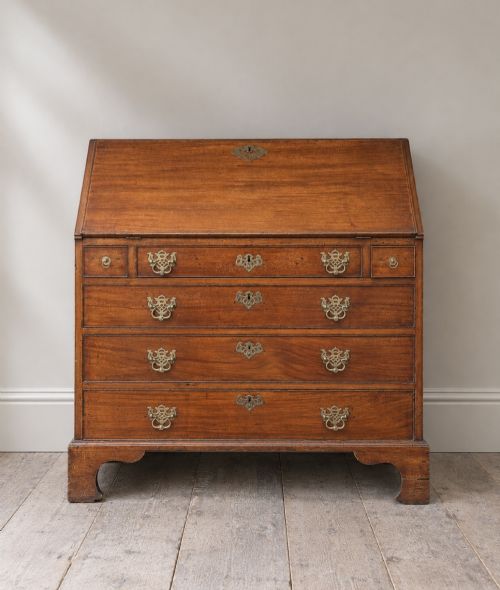 fig 1. An 18th-century Georgian mahogany slant-front bureau shown open, featuring a fitted interior with small drawers and pigeonholes above three long drawers with brass handles, resting on bracket feet.