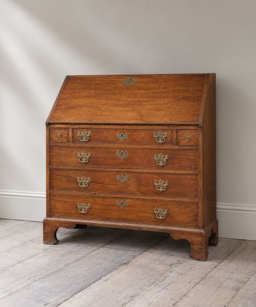fig 2. An 18th-century Georgian mahogany slant-front bureau shown open, featuring a fitted interior with small drawers and pigeonholes above three long drawers with brass handles, resting on bracket feet.
