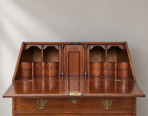 fig 3. An 18th-century Georgian mahogany slant-front bureau shown open, featuring a fitted interior with small drawers and pigeonholes above three long drawers with brass handles, resting on bracket feet.