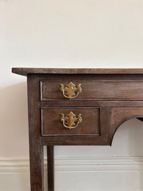 fig 1. An early eighteenth-century oak lowboy side table featuring one wide upper drawer, two small side drawers, an arched apron, brass handles, and straight square legs.