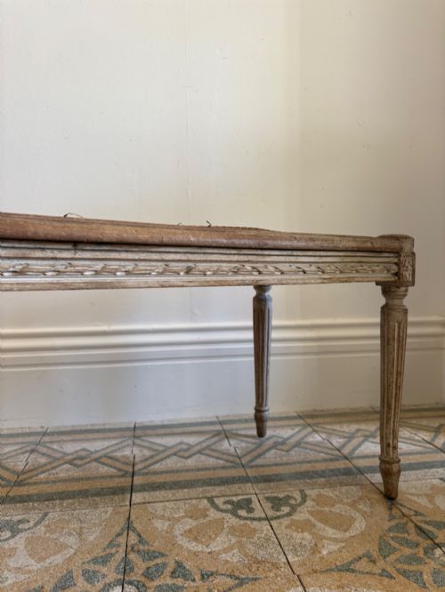 fig 2. A French Neoclassical rectangular stool featuring a distressed white painted finish, fluted tapered legs, carved rosette corner details, and a woven cane seat.