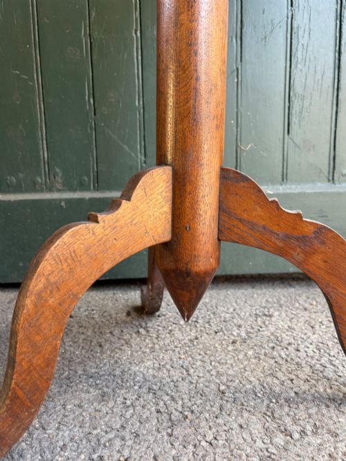 fig 1. An English Arts and Crafts solid oak wine table featuring a circular top, an under-top support bracket, a central column terminating in a pointed lower finial, and three splayed cabriole legs.