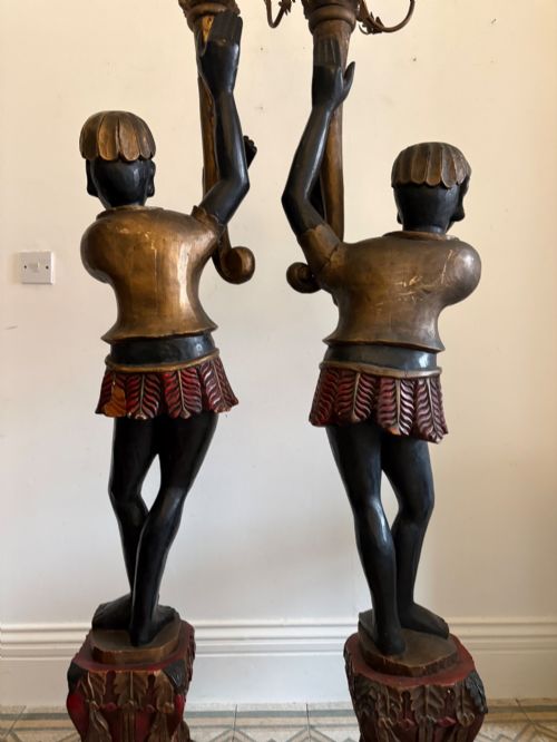 fig 2. A pair of life-sized Venetian carved wood figure floor lamps featuring gilt and polychrome details, mounted on ornate pedestals with multi-light metal candelabra tops.