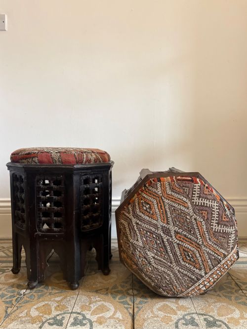 fig 4. A pair of dark wood octagonal stools with turned latticework side panels, arch-cut bases, and geometric woven kilim seat cushions.