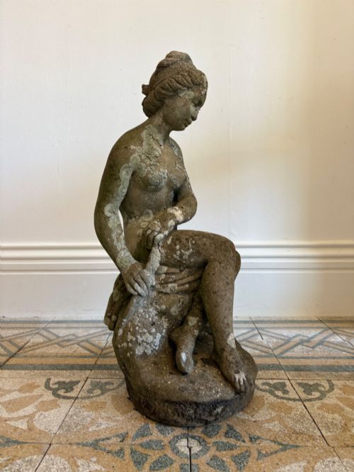 fig 1. A weathered cast stone statue depicting a seated classical female bather figure with a natural lichen patina.