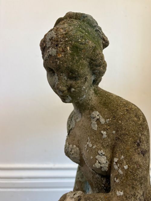 fig 2. A weathered cast stone statue depicting a seated classical female bather figure with a natural lichen patina.