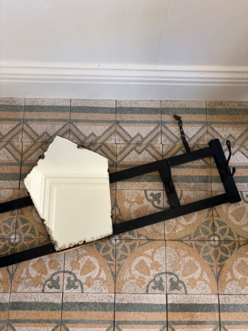 fig 1. A tall black wrought iron wall-mounted coat rack featuring integrated hooks, hanging chains, and an asymmetrical pentagonal mirror.