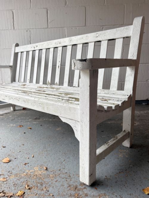 fig 1. An early 20th-century teak garden bench with a vertical slatted backrest, flat armrests, and a weathered white painted finish.