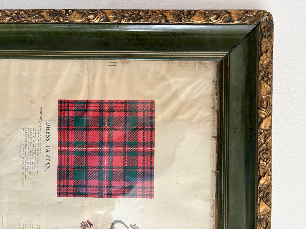 A large, vertically orientated framed paper genealogy chart for Clan Mackinnon featuring two tartan swatches and a central heraldic coat of arms at the top within a dark green and gilt wood frame. View VII