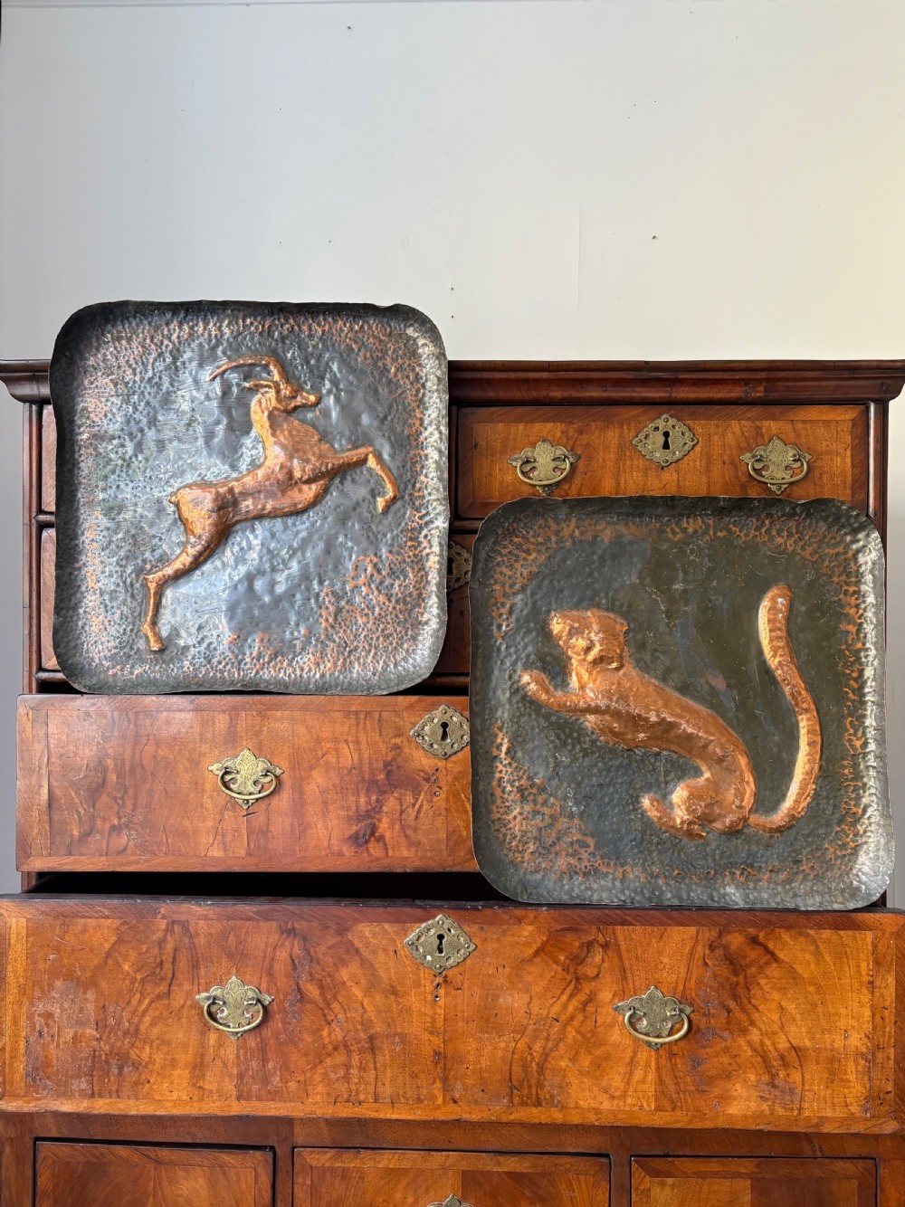 A pair of square late 19th-century hammered metal trays with raised repousse animal figures of an ibex and a feline.