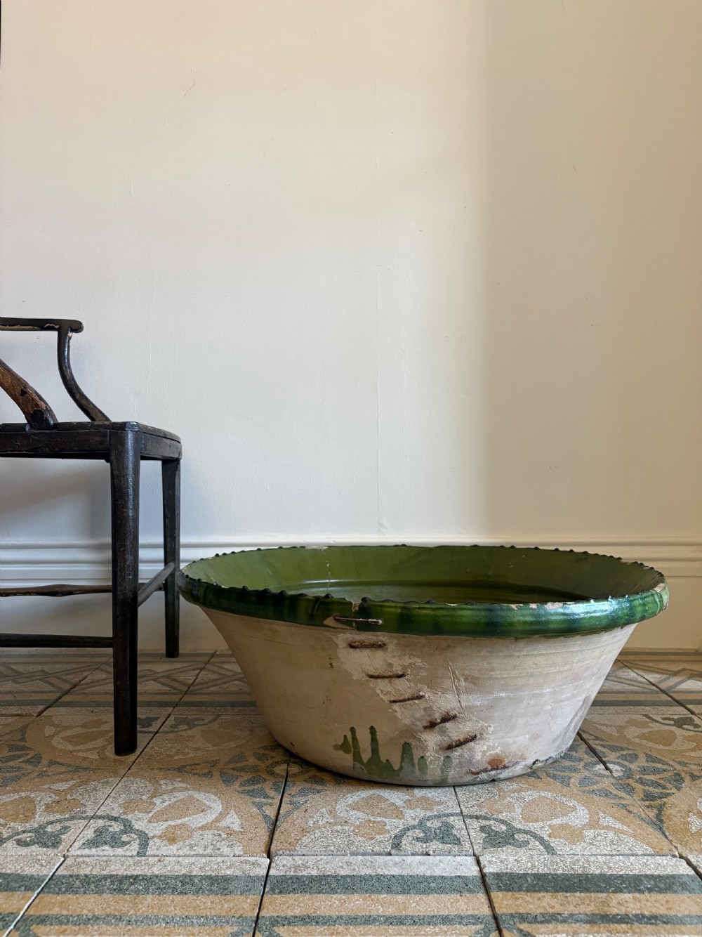 A large 19th-century French earthenware tian bowl featuring an unglazed cream exterior with historical iron staple repairs and a green-glazed interior.