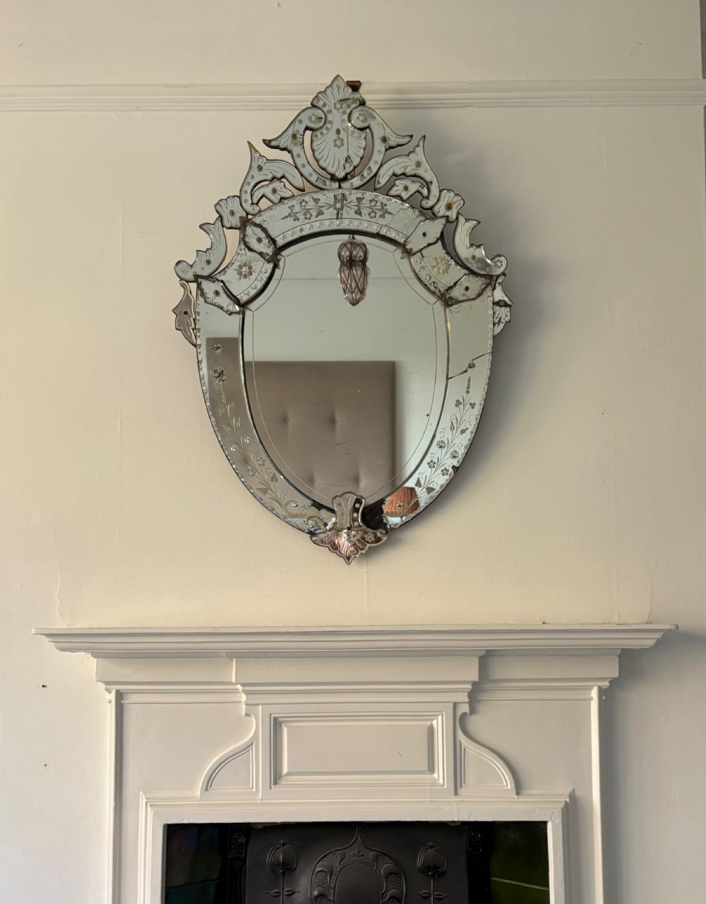 An oval Venetian wall mirror featuring an etched glass frame with floral motifs, a scrollwork crest, and a bevelled centre mirror with light foxing. View II