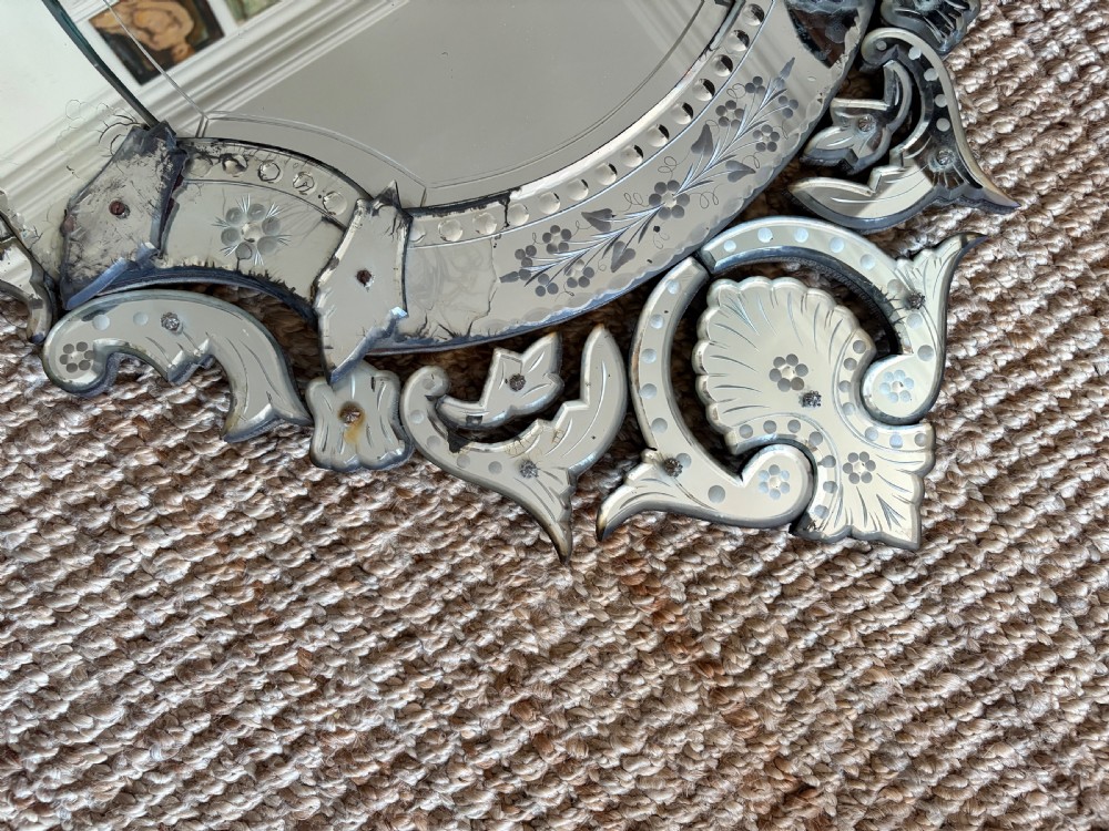 An oval Venetian wall mirror featuring an etched glass frame with floral motifs, a scrollwork crest, and a bevelled centre mirror with light foxing. View VII