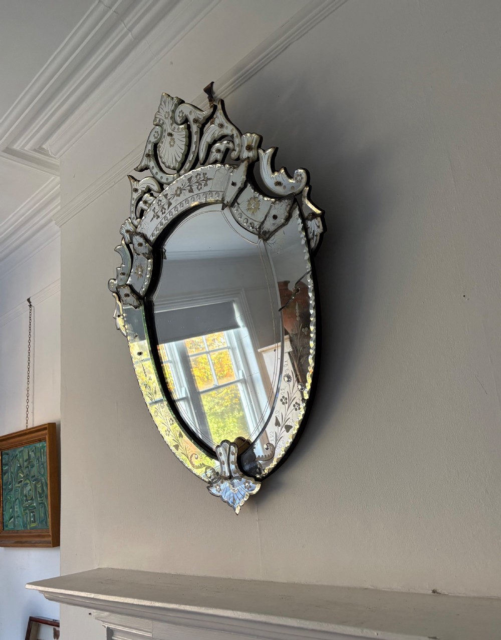An oval Venetian wall mirror featuring an etched glass frame with floral motifs, a scrollwork crest, and a bevelled centre mirror with light foxing. View XIII