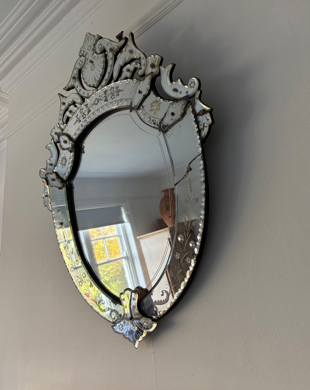 An oval Venetian wall mirror featuring an etched glass frame with floral motifs, a scrollwork crest, and a bevelled centre mirror with light foxing. View XVI