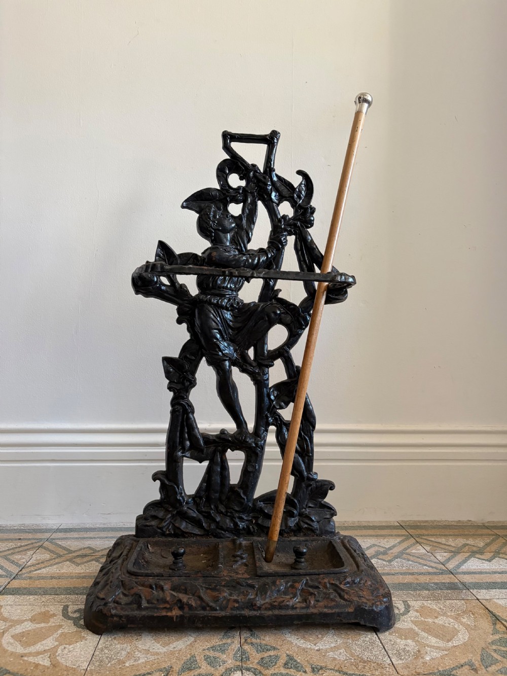 A black cast iron stick stand featuring a relief depiction of Jack climbing a beanstalk above a twin drip tray base.
