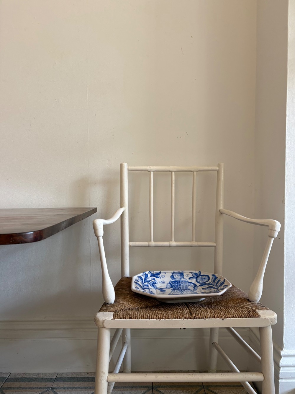 A white painted 19th-century turned wood armchair with a spindle back, curved armrests, and a natural woven rush seat. View II