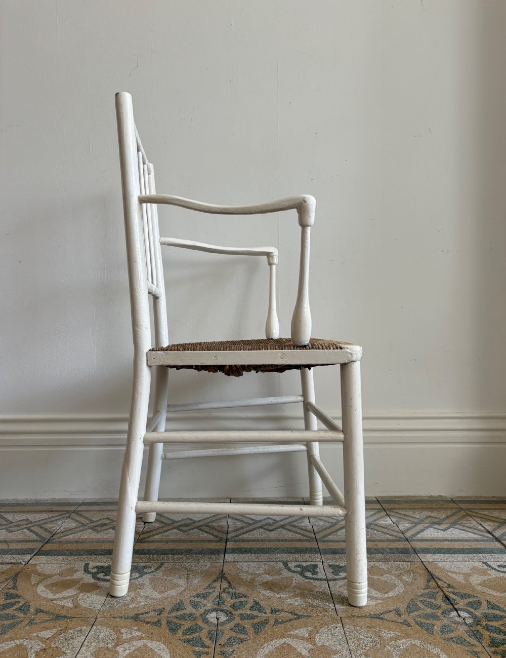 A white painted 19th-century turned wood armchair with a spindle back, curved armrests, and a natural woven rush seat. View VI
