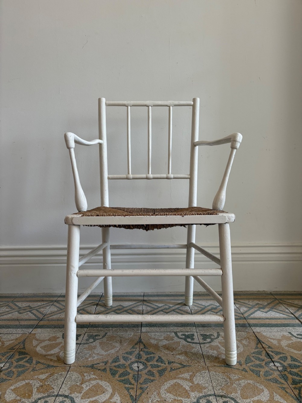 A white painted 19th-century turned wood armchair with a spindle back, curved armrests, and a natural woven rush seat.