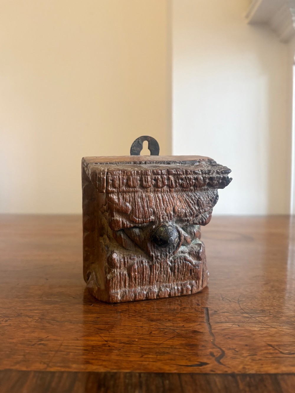 A small hand-carved dark oak architectural fragment featuring relief detail and a metal mounting loop at the top.