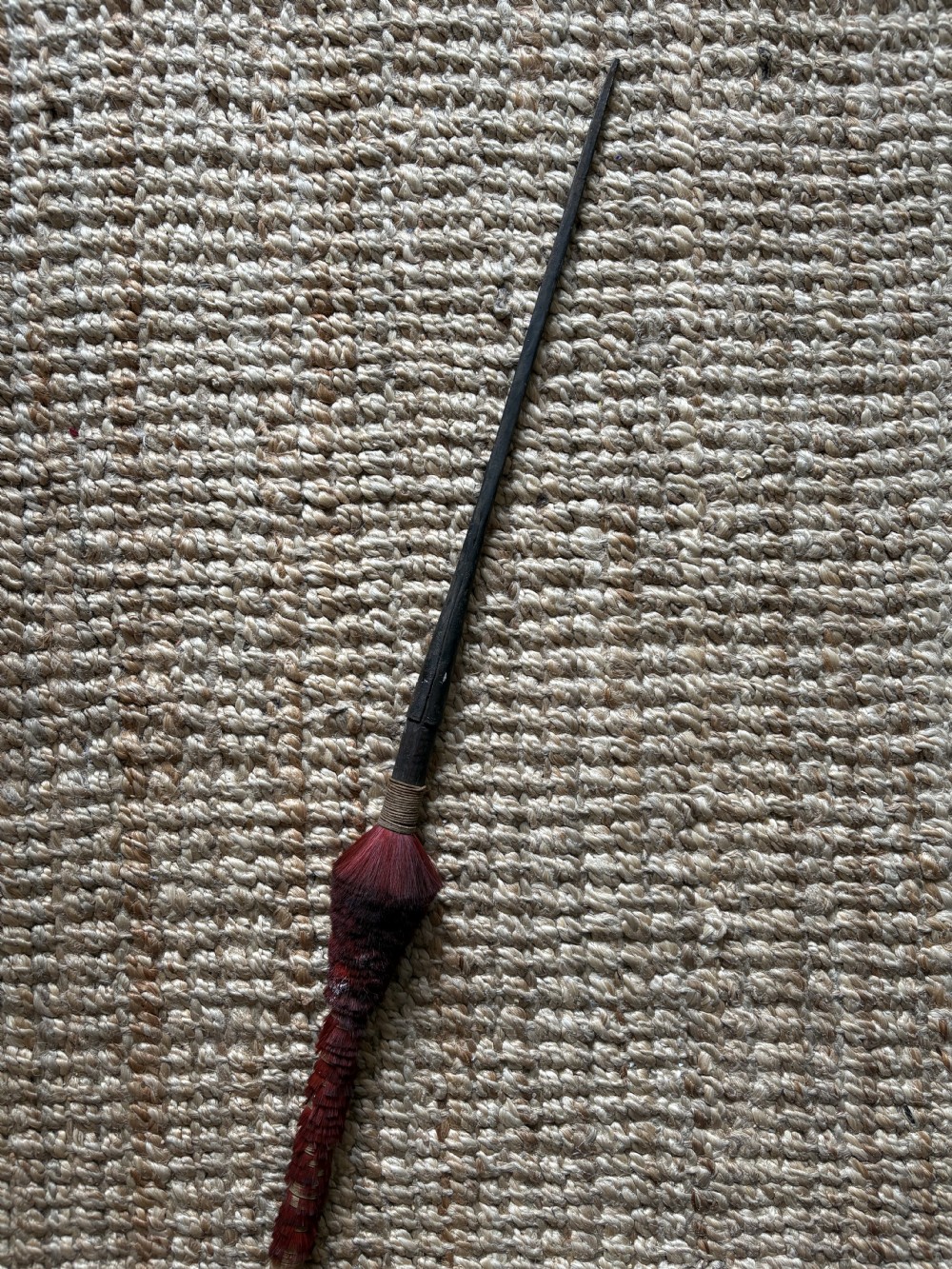 A 19th-century African Zulu iron spear featuring an elongated dark forged blade and a shaft wrapped in crimson vegetable-dyed bristles.