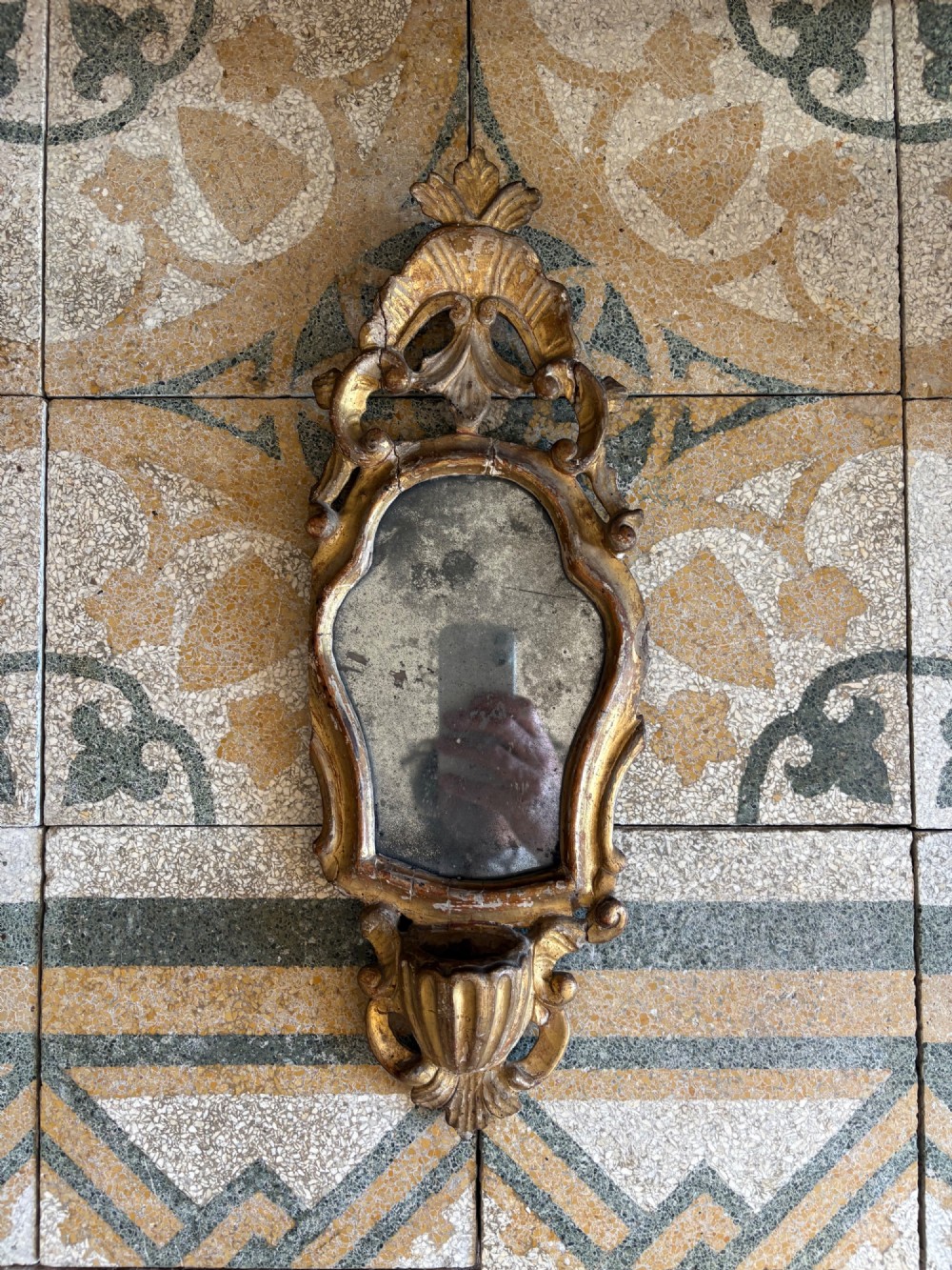 An 18th-century Italian Rococo carved giltwood cartouche wall mirror featuring ornate scrollwork, an upper crest, and a heavily foxed mirror glass plate. View II