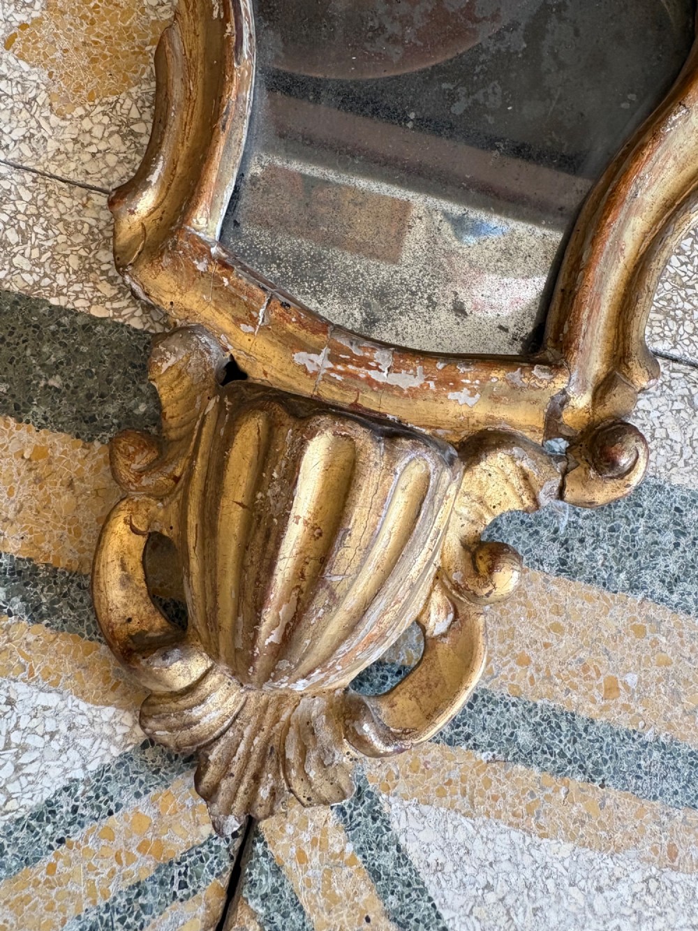 An 18th-century Italian Rococo carved giltwood cartouche wall mirror featuring ornate scrollwork, an upper crest, and a heavily foxed mirror glass plate. View III