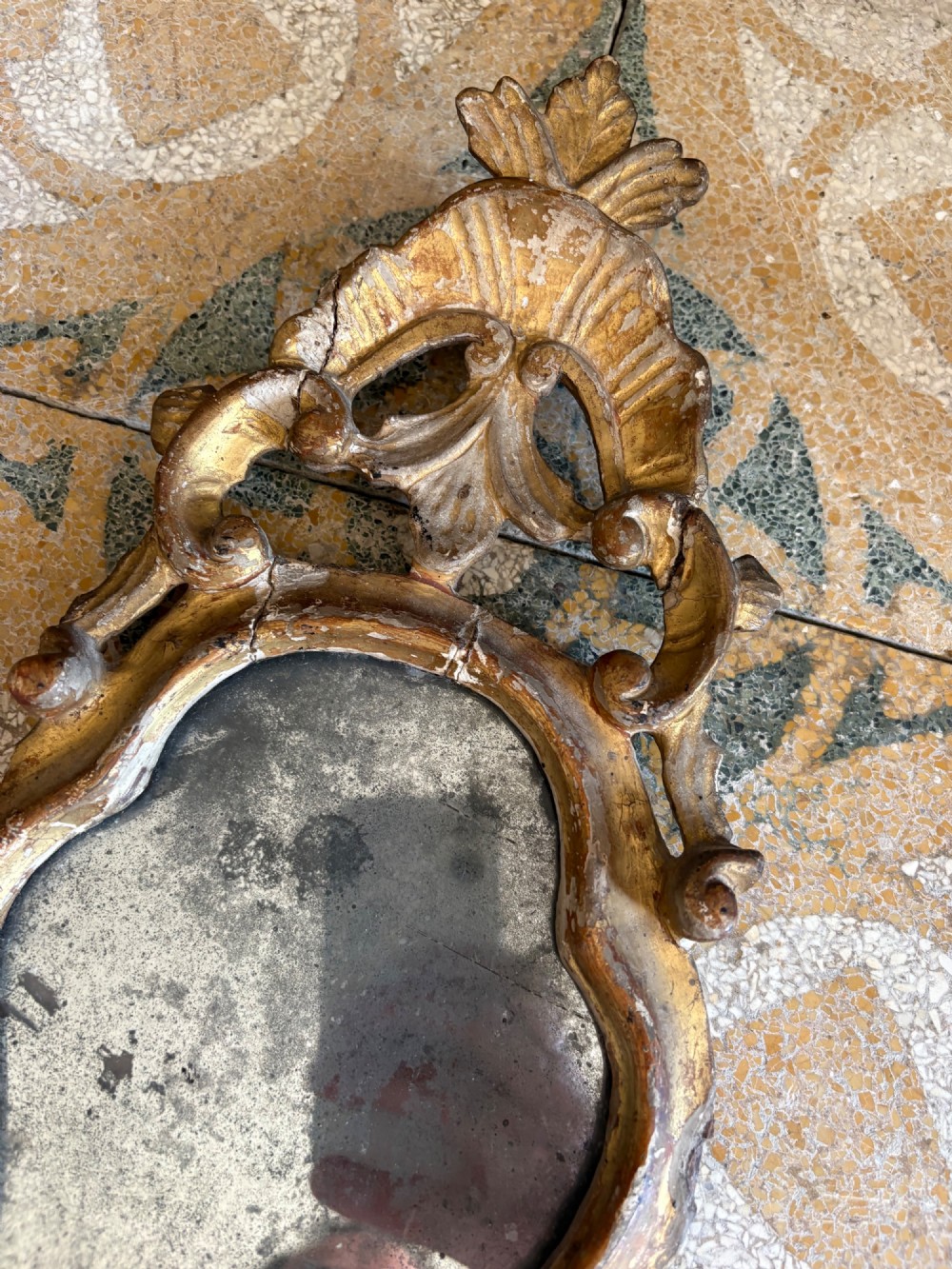 An 18th-century Italian Rococo carved giltwood cartouche wall mirror featuring ornate scrollwork, an upper crest, and a heavily foxed mirror glass plate. View IV