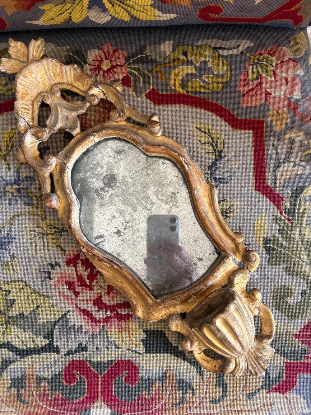 An 18th-century Italian Rococo carved giltwood cartouche wall mirror featuring ornate scrollwork, an upper crest, and a heavily foxed mirror glass plate. View IX