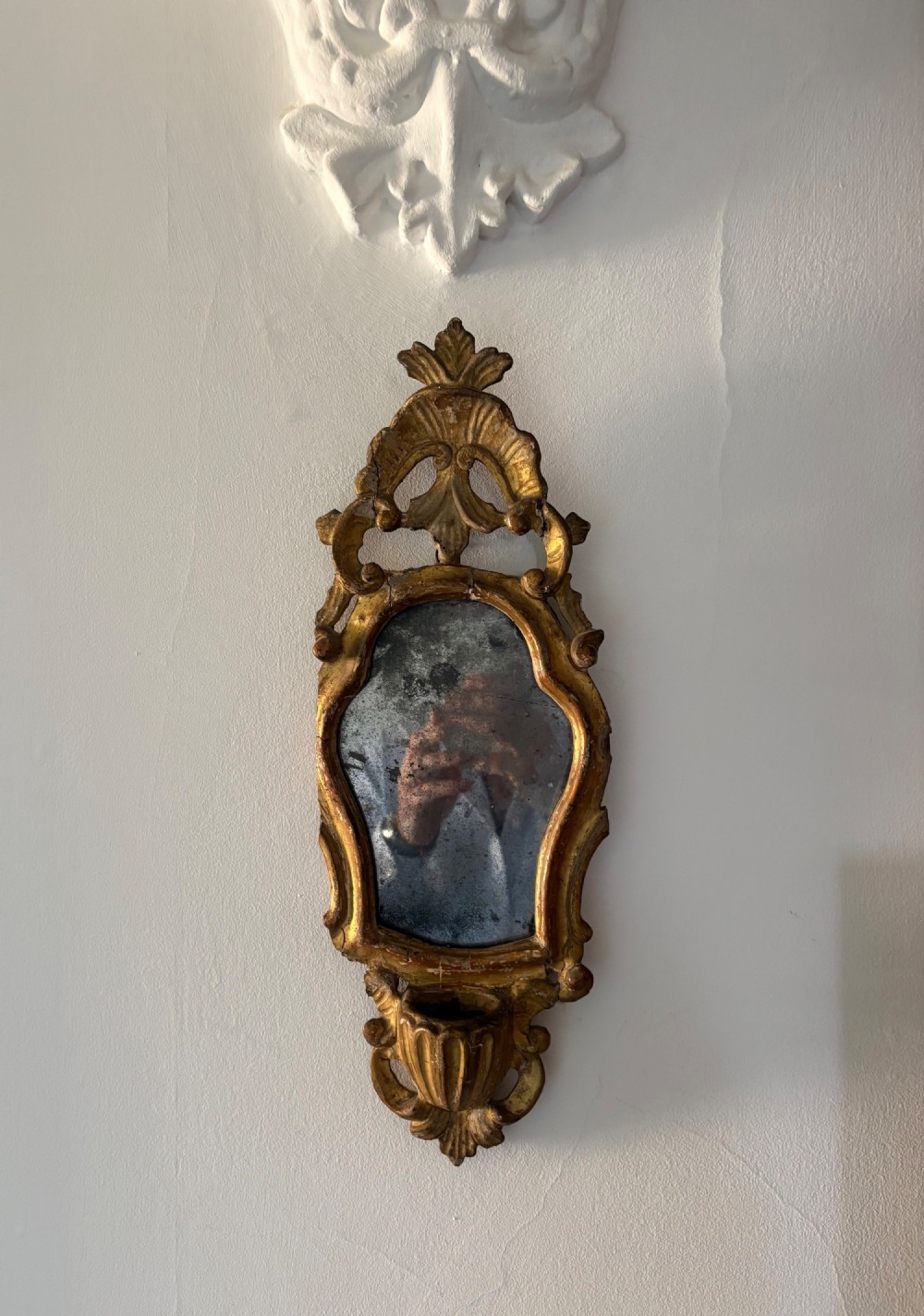 An 18th-century Italian Rococo carved giltwood cartouche wall mirror featuring ornate scrollwork, an upper crest, and a heavily foxed mirror glass plate.