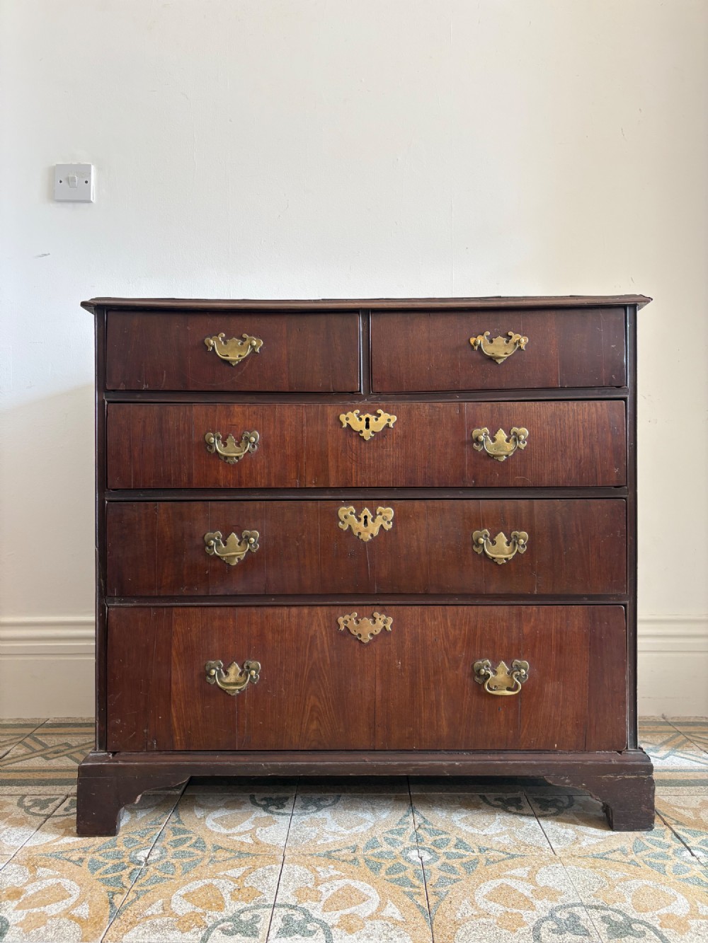 A mid-18th-century Georgian walnut chest of drawers featuring a two-over-three drawer layout, brass handles with backplates, and bracket feet.