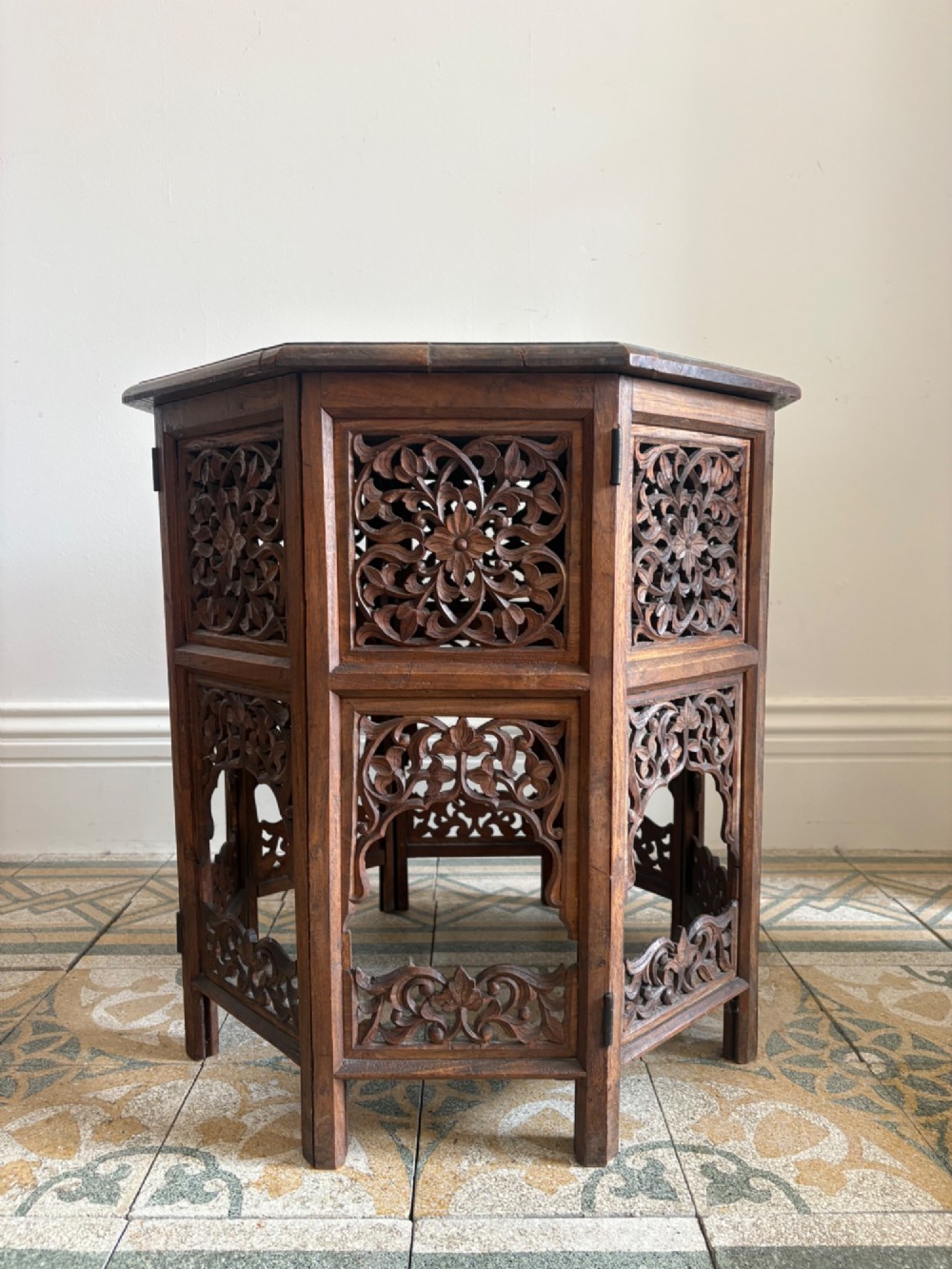 An octagonal dark teak side table featuring intricate openwork floral carving and arched fretwork base panels.