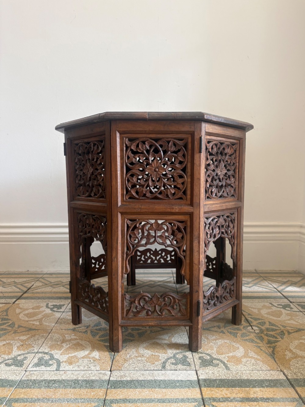 An octagonal dark teak side table featuring intricate openwork floral carving and arched fretwork base panels. View IV