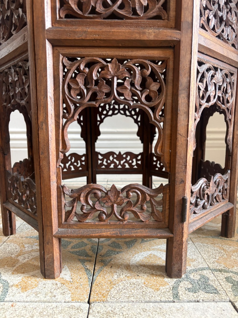 An octagonal dark teak side table featuring intricate openwork floral carving and arched fretwork base panels. View VI