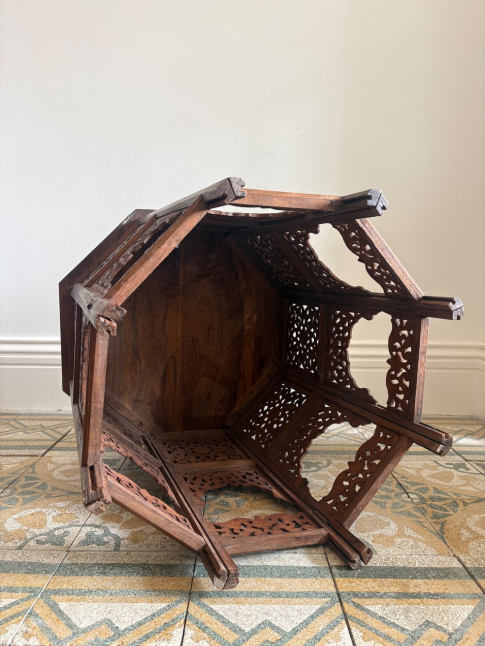 An octagonal dark teak side table featuring intricate openwork floral carving and arched fretwork base panels. View VIII