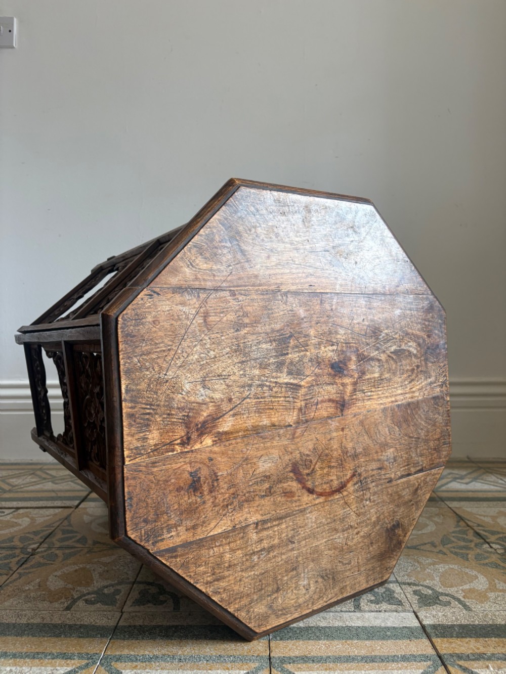An octagonal dark teak side table featuring intricate openwork floral carving and arched fretwork base panels. View IX